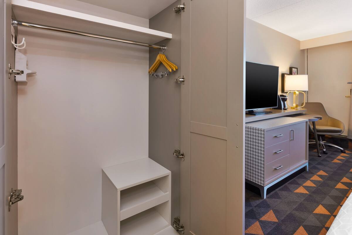 Une chambre d’hôtel équipée d’une armoire, d’une télévision, d’un bureau avec une lampe et d’un tapis à motifs.
