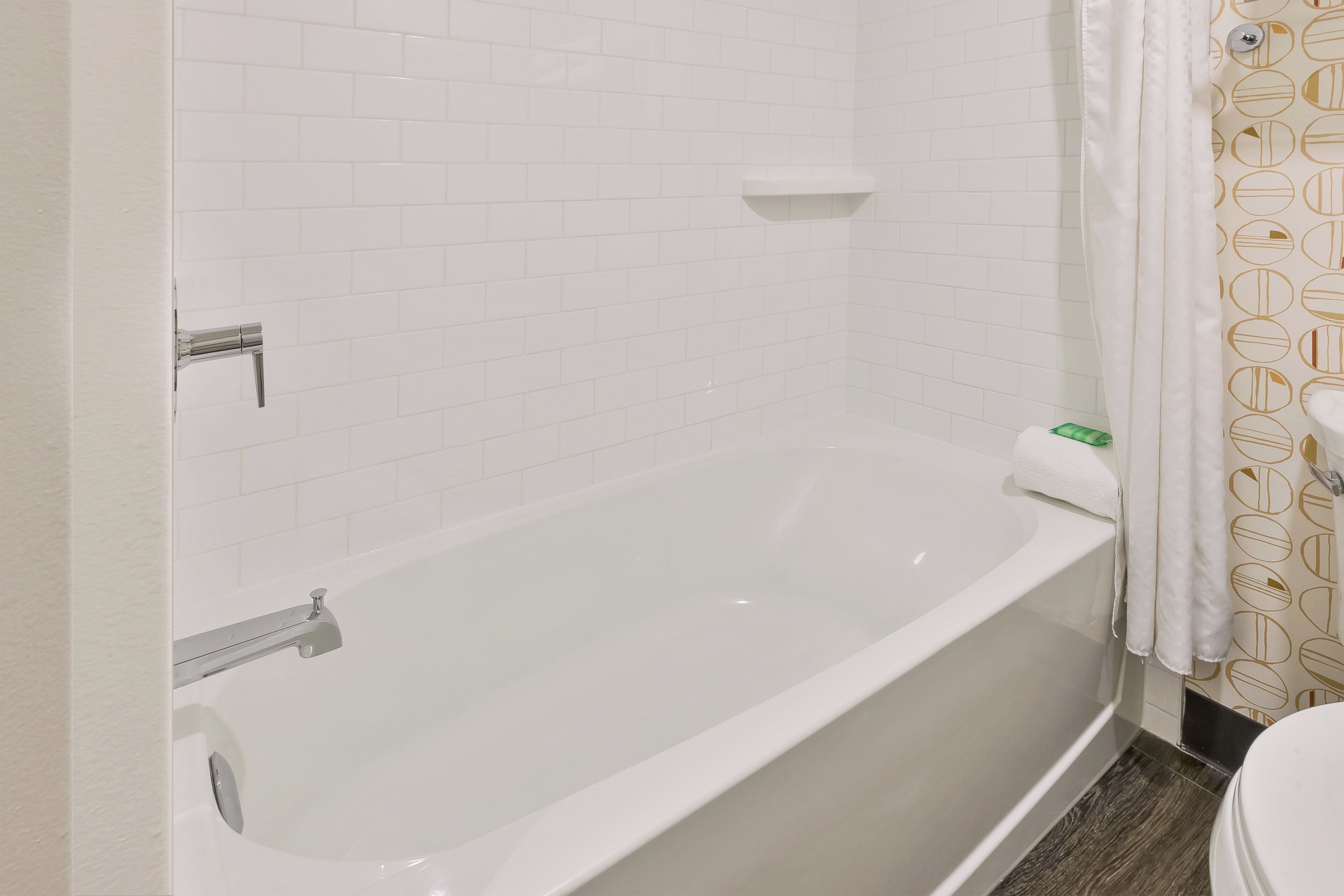 A bathroom with a white bathtub, a white toilet, and a shower curtain with a geometric pattern.