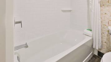 A bathroom with a white bathtub, a white toilet, and a shower curtain with a geometric pattern.