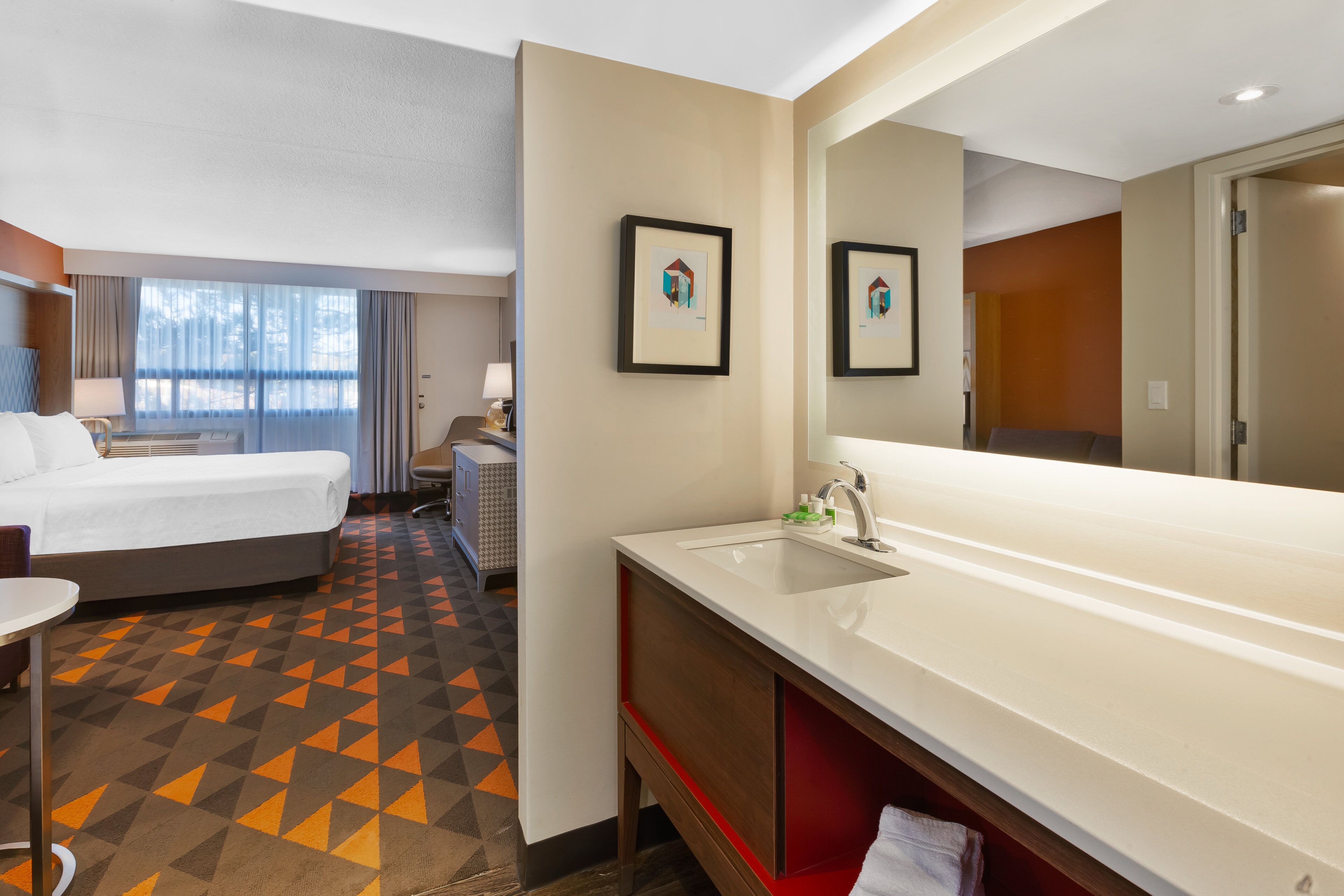 A hotel room with a bed, a large bathroom with a sink and mirror, and a small table.