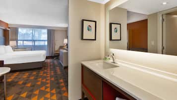 A hotel room with a bed, a large bathroom with a sink and mirror, and a small table.