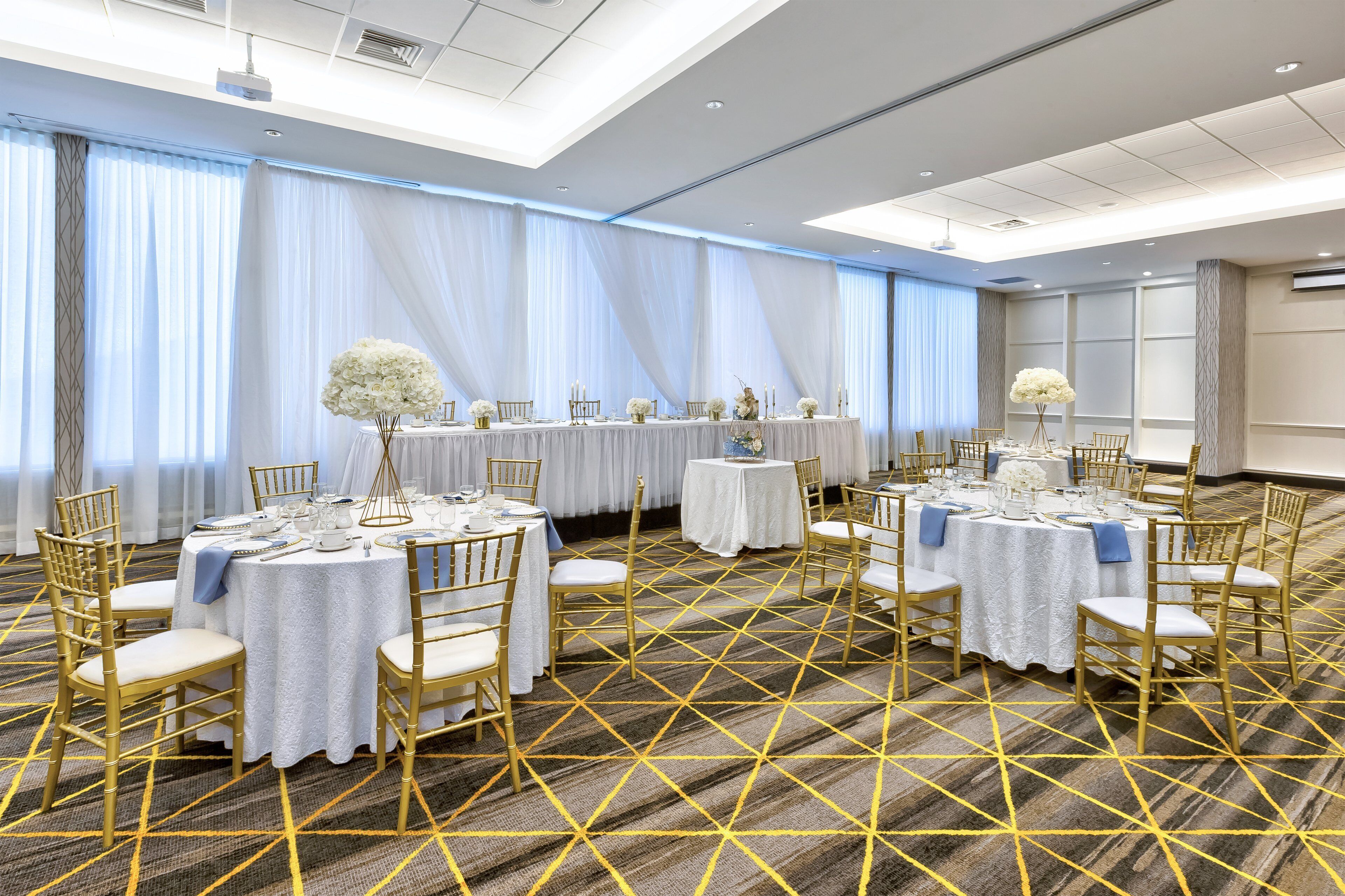A conference room with round tables, white tablecloths, gold chairs, and a geometric carpet pattern.