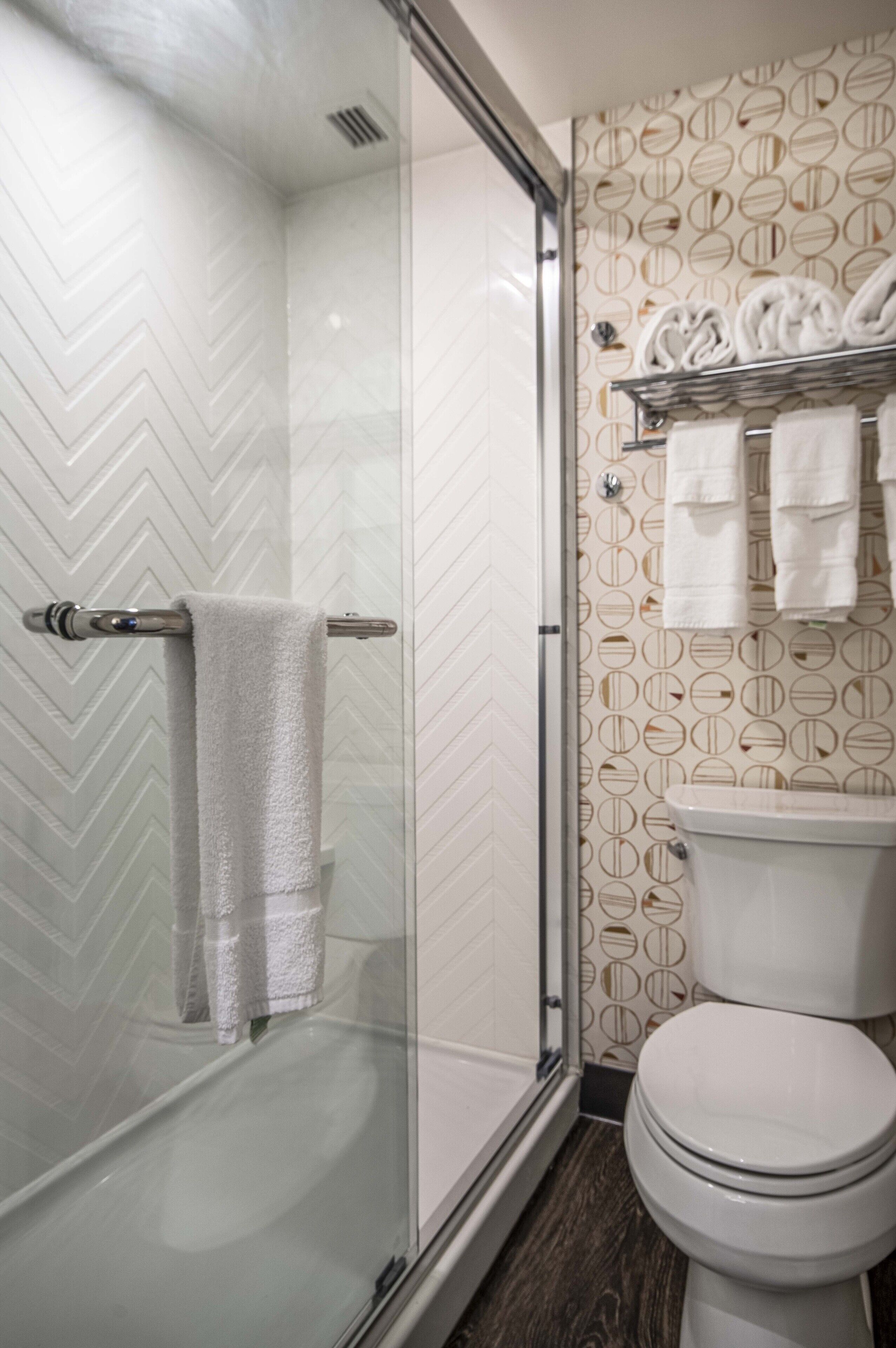 A modern bathroom with a glass shower enclosure, a toilet, and a towel rack with multiple towels.