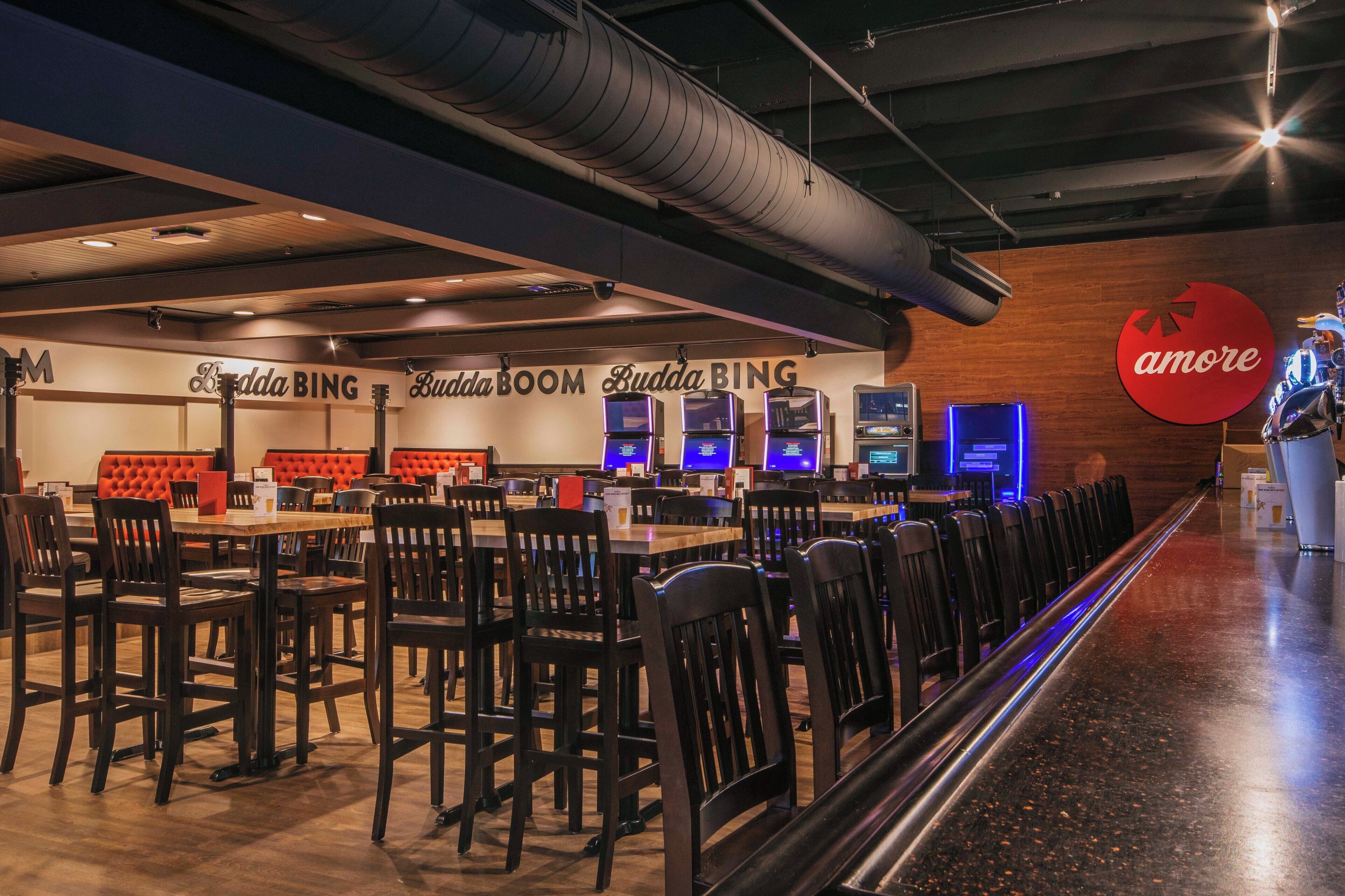 A restaurant with multiple tables and chairs, a bar area with stools, and a large red logo on the wall.