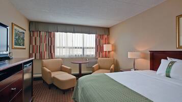 A hotel room with a bed, two armchairs, a desk with a television, a lamp, and a window with curtains.