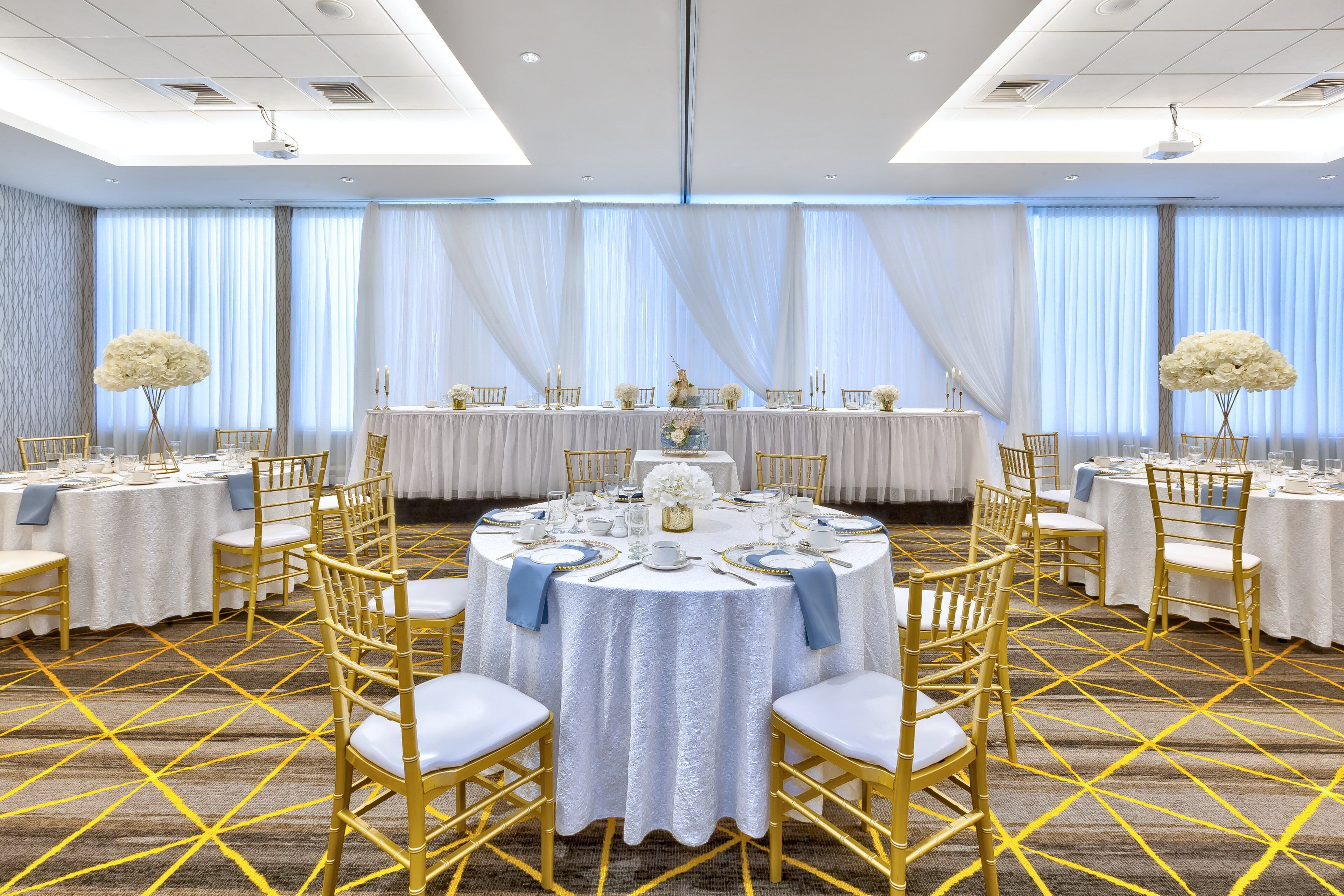 A banquet hall with round tables set for dining, gold chairs, and white tablecloths.