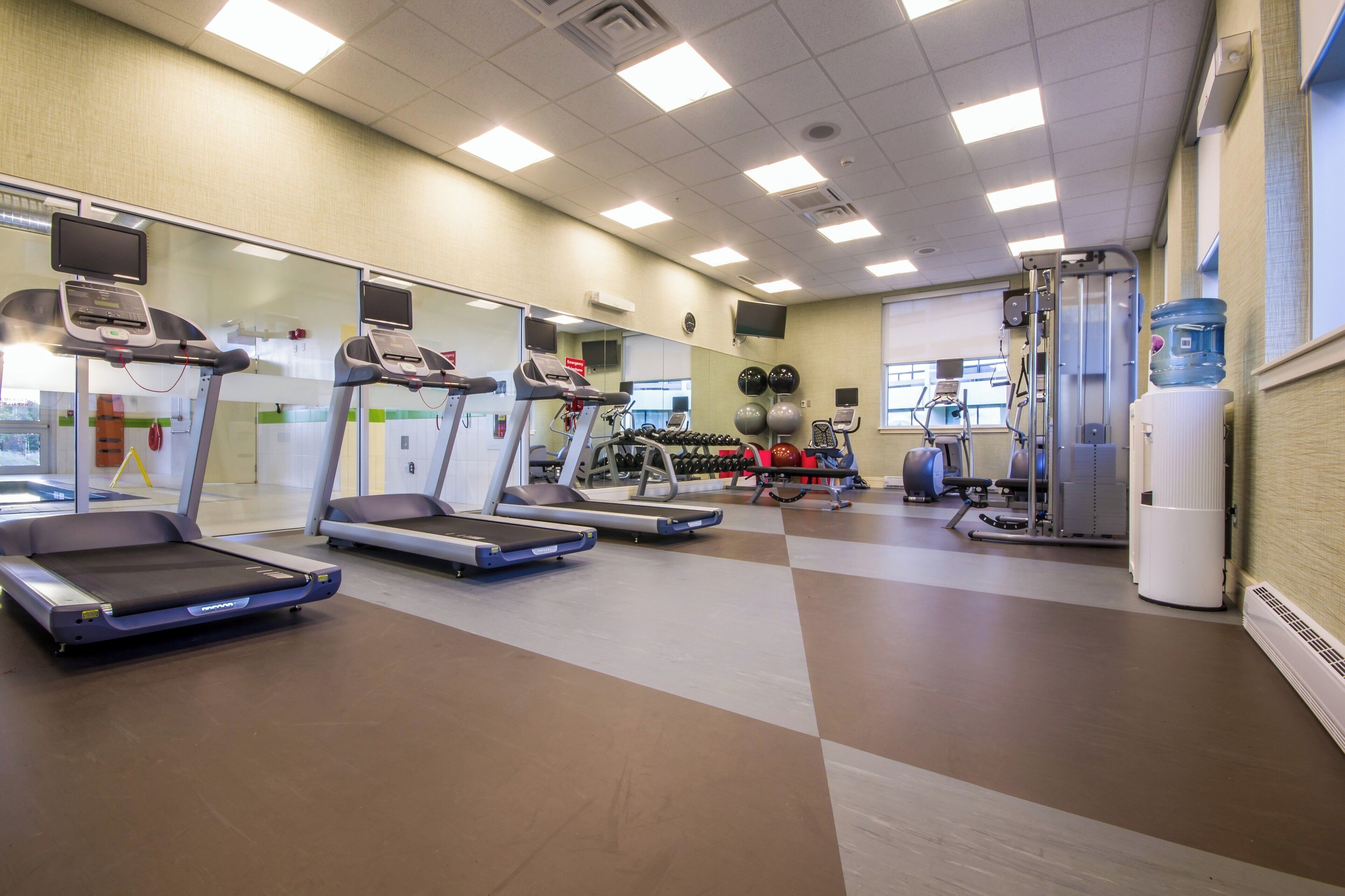 Un gimnasio con cintas de correr, máquinas de pesas y un dispensador de agua.