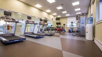 Un gimnasio con cintas de correr, máquinas de pesas y un dispensador de agua.