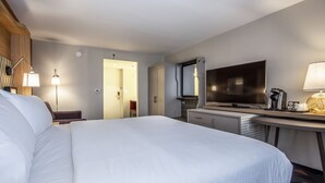 Habitació d'hotel amb un llit gran, una taula de treball, un televisor de pantalla plana, una làmpada i una cafetera.