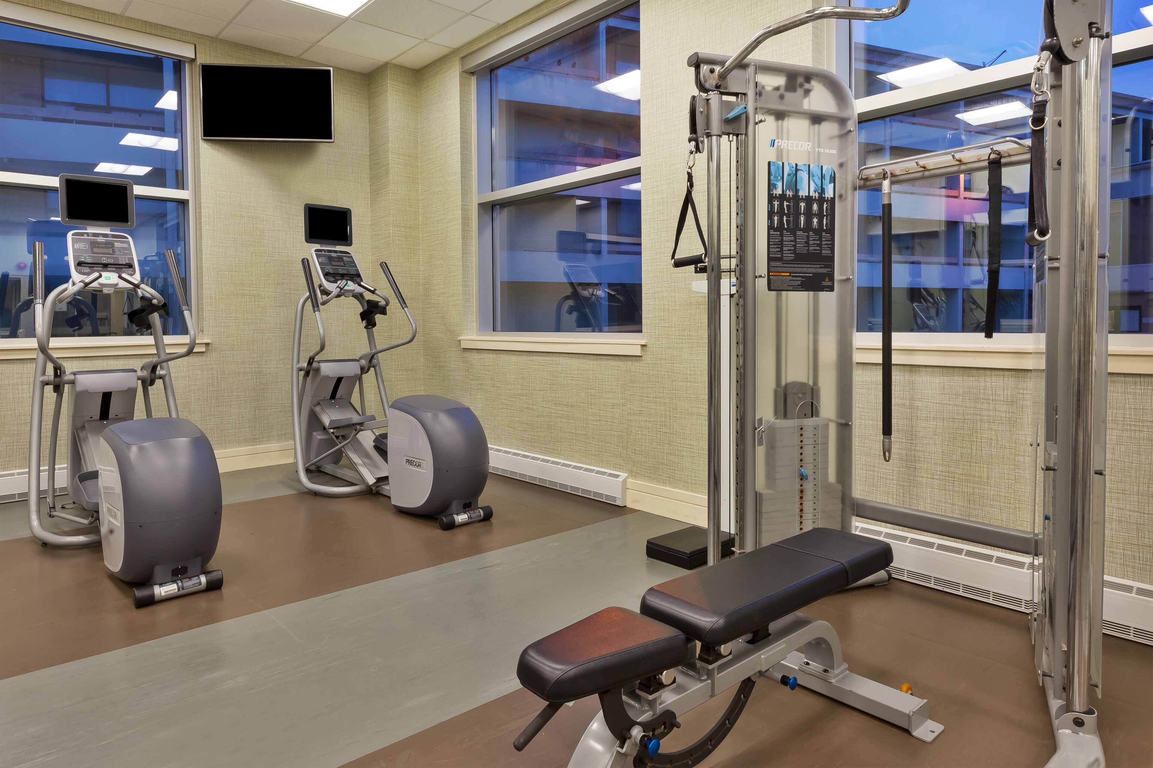 A gym with exercise equipment, a bench, and large windows.