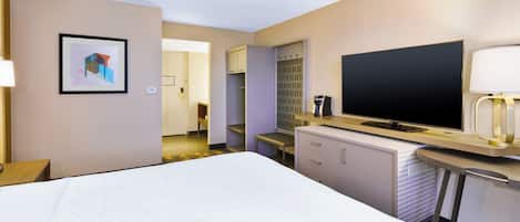 Una habitación de hotel con cama, televisor de pantalla plana, escritorio con lámpara, espejo y un cuadro en la pared.