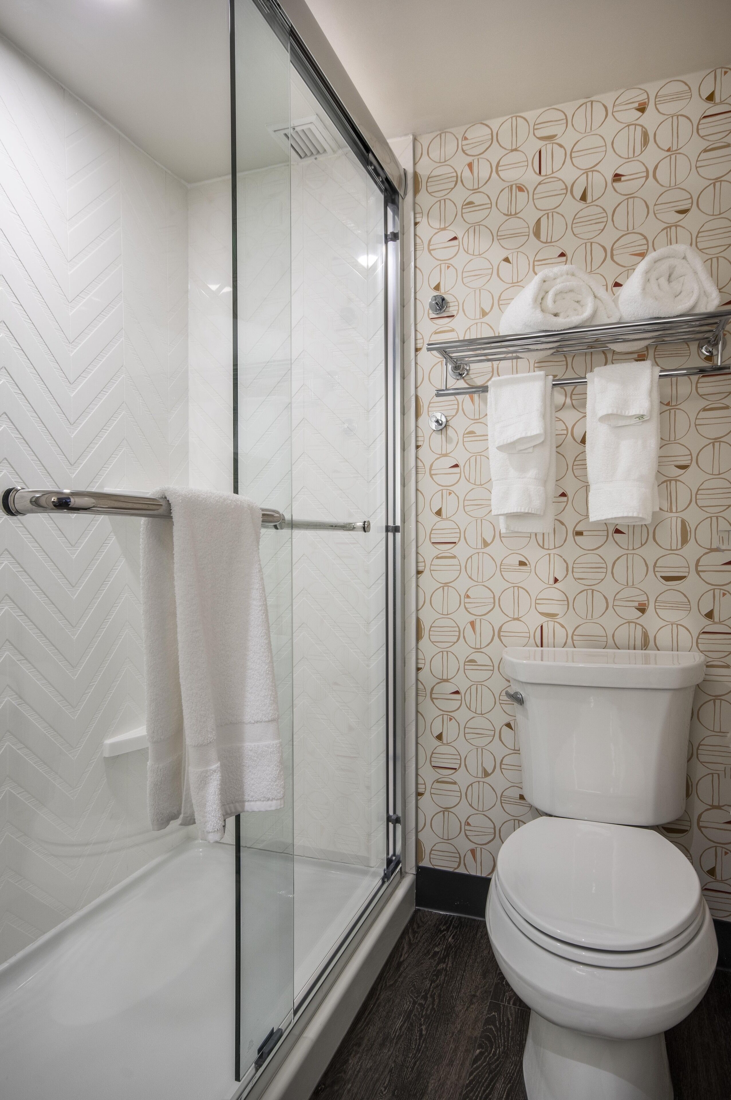A modern bathroom with a glass-enclosed shower, a white toilet, and a towel rack with towels.