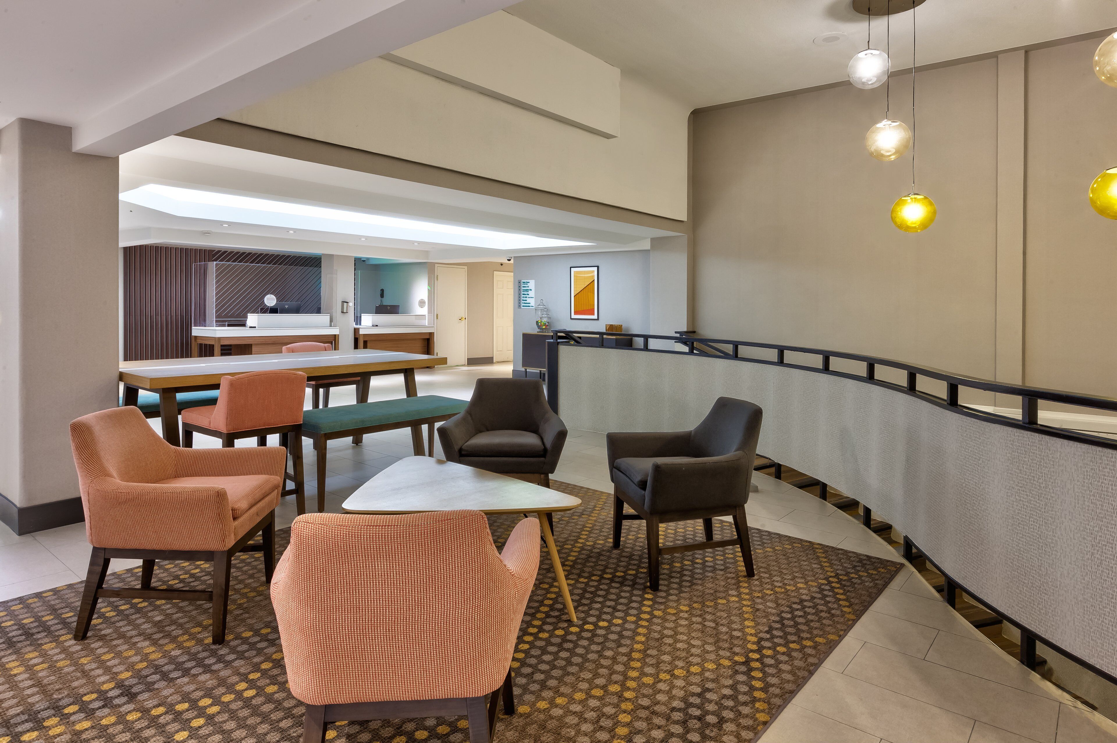 A modern hotel lobby with seating, a reception desk, and a staircase.