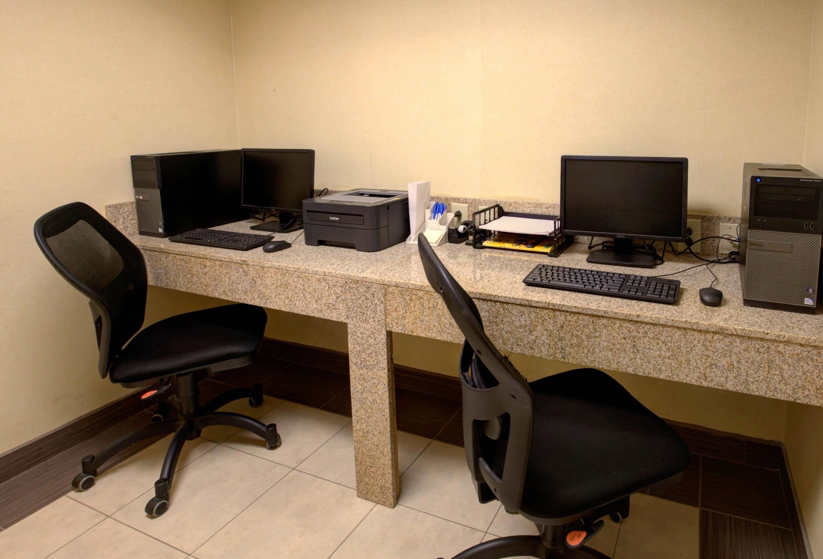 A workspace with two desks, each equipped with a computer, keyboard, and monitor. There are two office chairs, one on each desk.