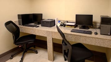 A workspace with two desks, each equipped with a computer, keyboard, and monitor. There are two office chairs, one on each desk.