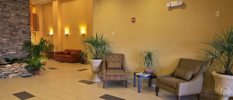 Un vestíbulo con pared de ladrillo, dos sillones, un sofá y plantas en macetas.