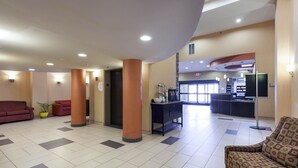 Un hall d’entrée comprenant un comptoir de réception, un espace où l’on peut se servir du café, et un coin salon avec un canapé rouge et un fauteuil à motifs.