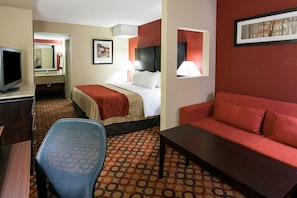 Een hotelkamer met een bed, een bureau met een computer, een stoel, een bank en een kamerbreed tapijt met een patroon.