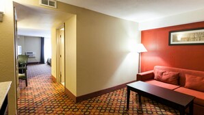 Une chambre d’hôtel avec un tapis à motifs, un canapé rouge, une petite table et une lampe.