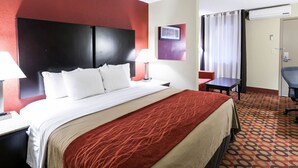 Une chambre d’hôtel avec un grand lit, deux tables de chevet avec des lampes, un petit bureau, une chaise et une porte avec des rideaux.