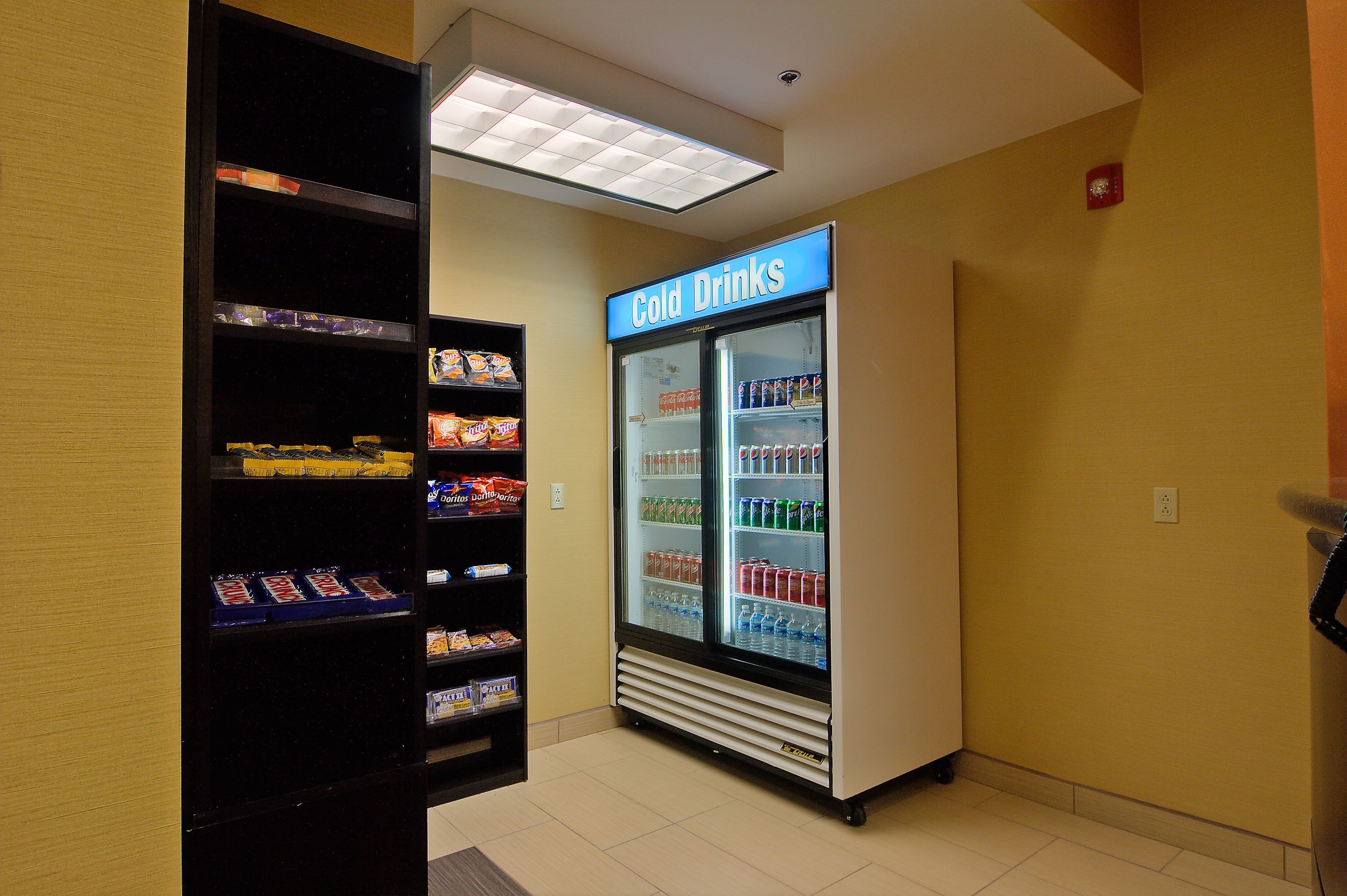Zona de máquinas expendedoras con un refrigerador que exhibe bebidas frías, con una variedad de opciones.