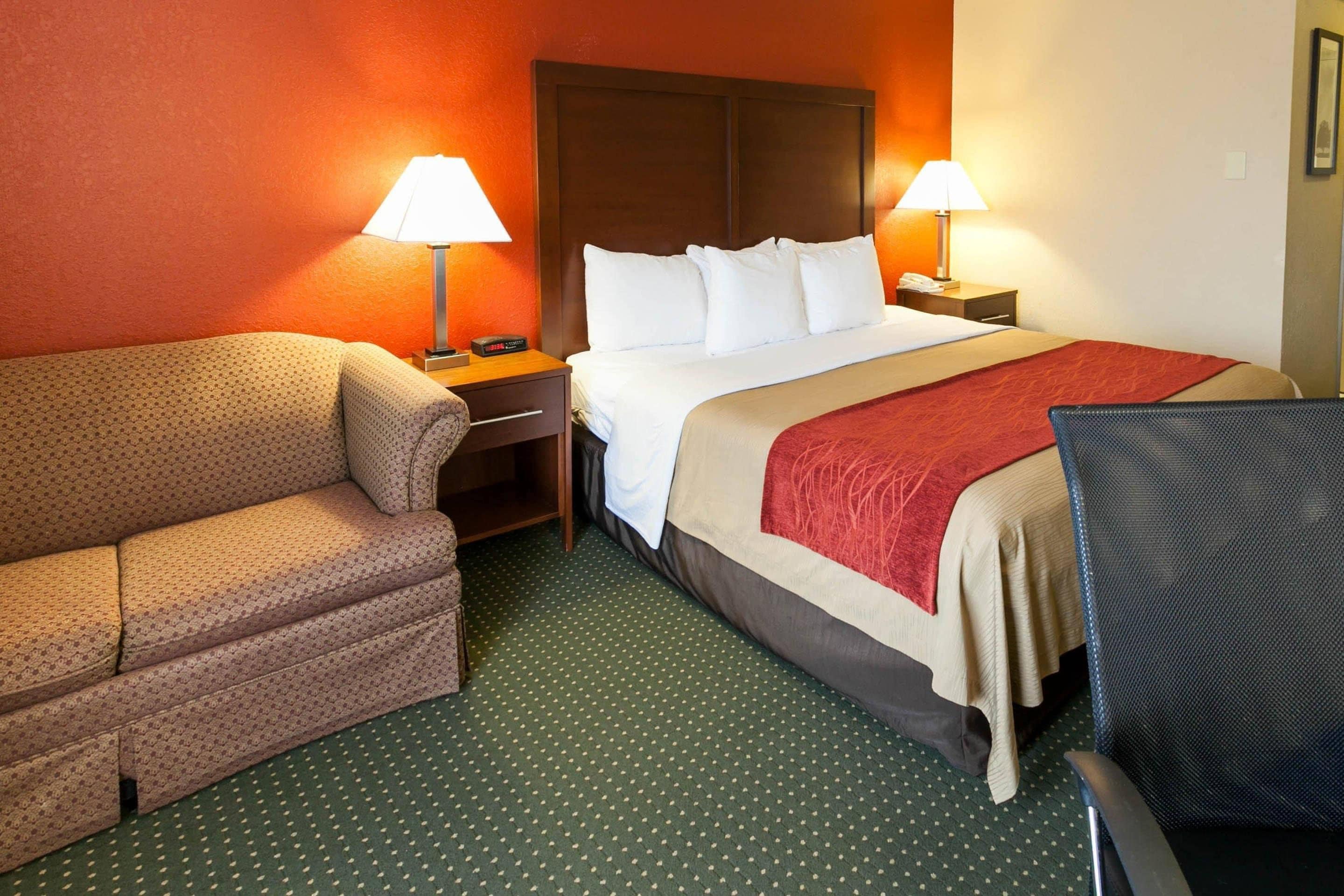 A hotel room with a bed, a sofa, a desk, and two lamps.