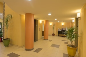 Un vestíbulo de hotel con pilares altos, plantas en macetas y una zona de recepción.