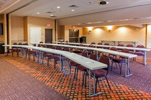 Une salle de conférence avec de longues tables et des chaises, un sol recouvert de moquette et des panneaux indicateurs de sortie.