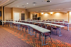 A conference room with long tables and chairs, carpeted floor, and exit signs.