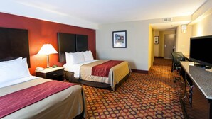 Une chambre d’hôtel avec deux lits, un bureau, une télévision et une moquette à motifs.