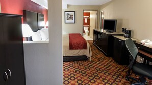 Une chambre d’hôtel avec un lit, un bureau équipé d’un ordinateur, une télévision et une salle de bain visible à travers une porte ouverte.