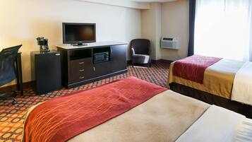 A hotel room with two beds, a desk with a television, a chair, and an air conditioning unit.