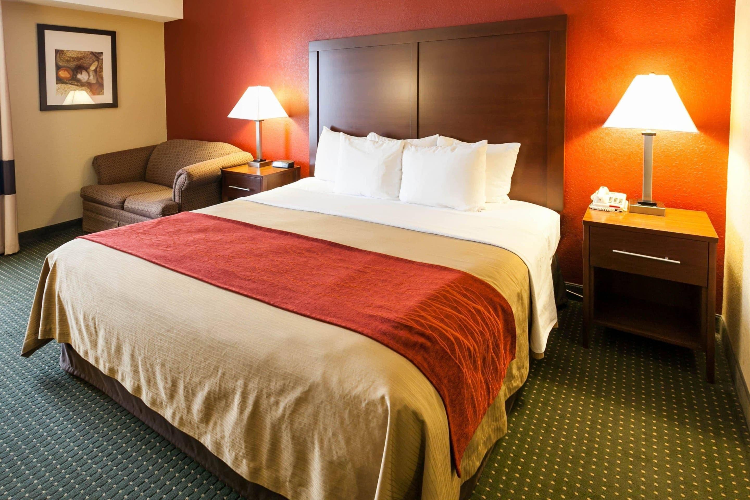 A hotel room with a large bed, two bedside tables, a chair, and a lamp.