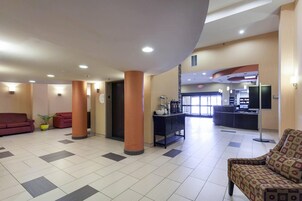 A lobby with a reception desk, a red sofa, a patterned armchair, and a potted plant.
