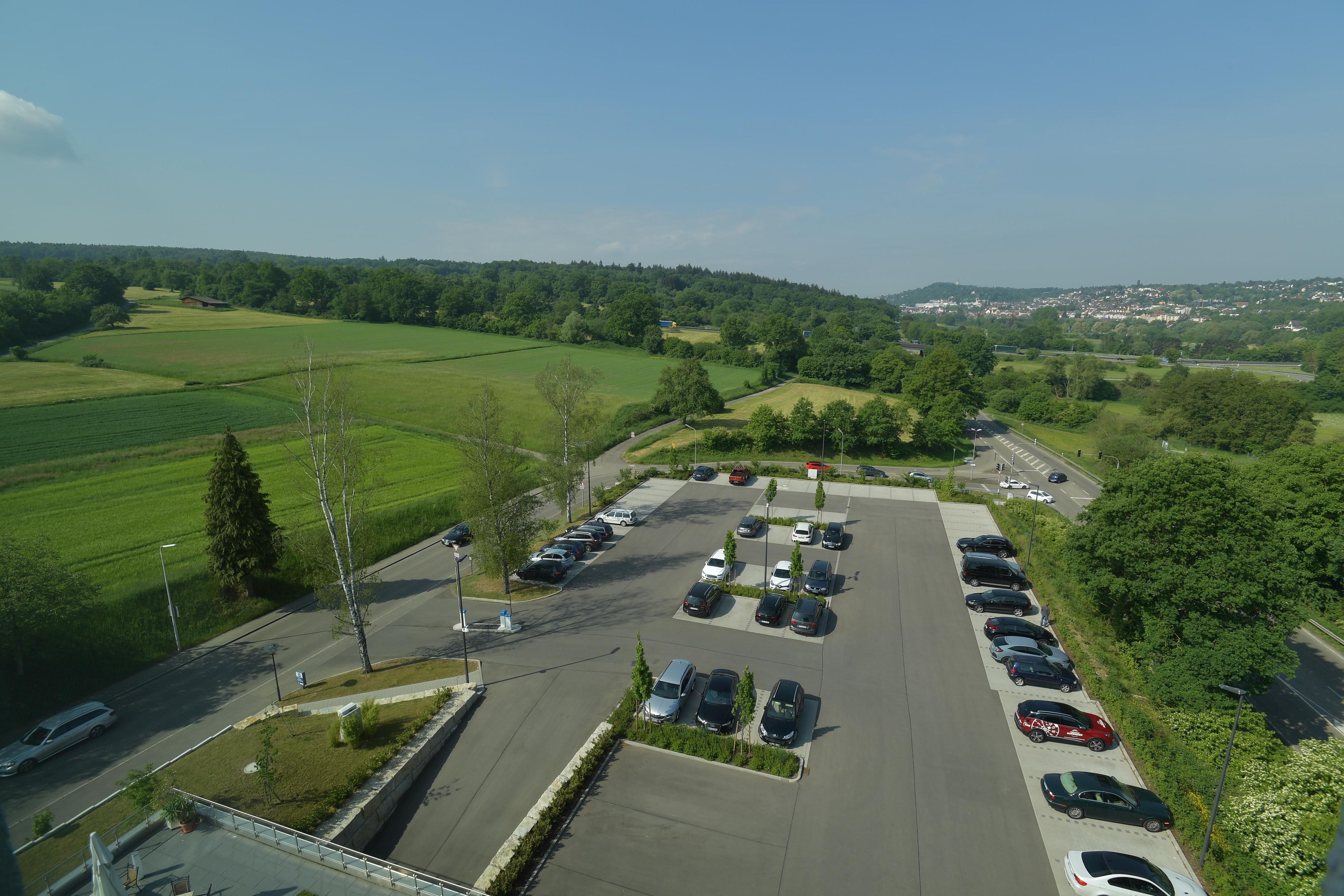 A parking lot with multiple cars, surrounded by green fields and trees.