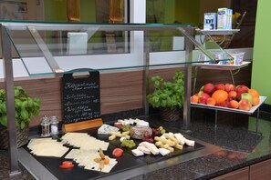 Eine Käse- und Obstauslage in einem Restaurant, durch eine Glasscheibe getrennt.