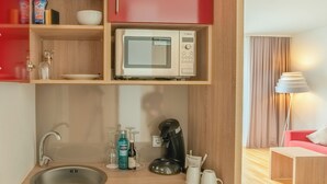 Eine kompakte Küchenzeile mit Mikrowelle, Kaffeemaschine und einem mit Getränken gefüllten Kühlschrank.