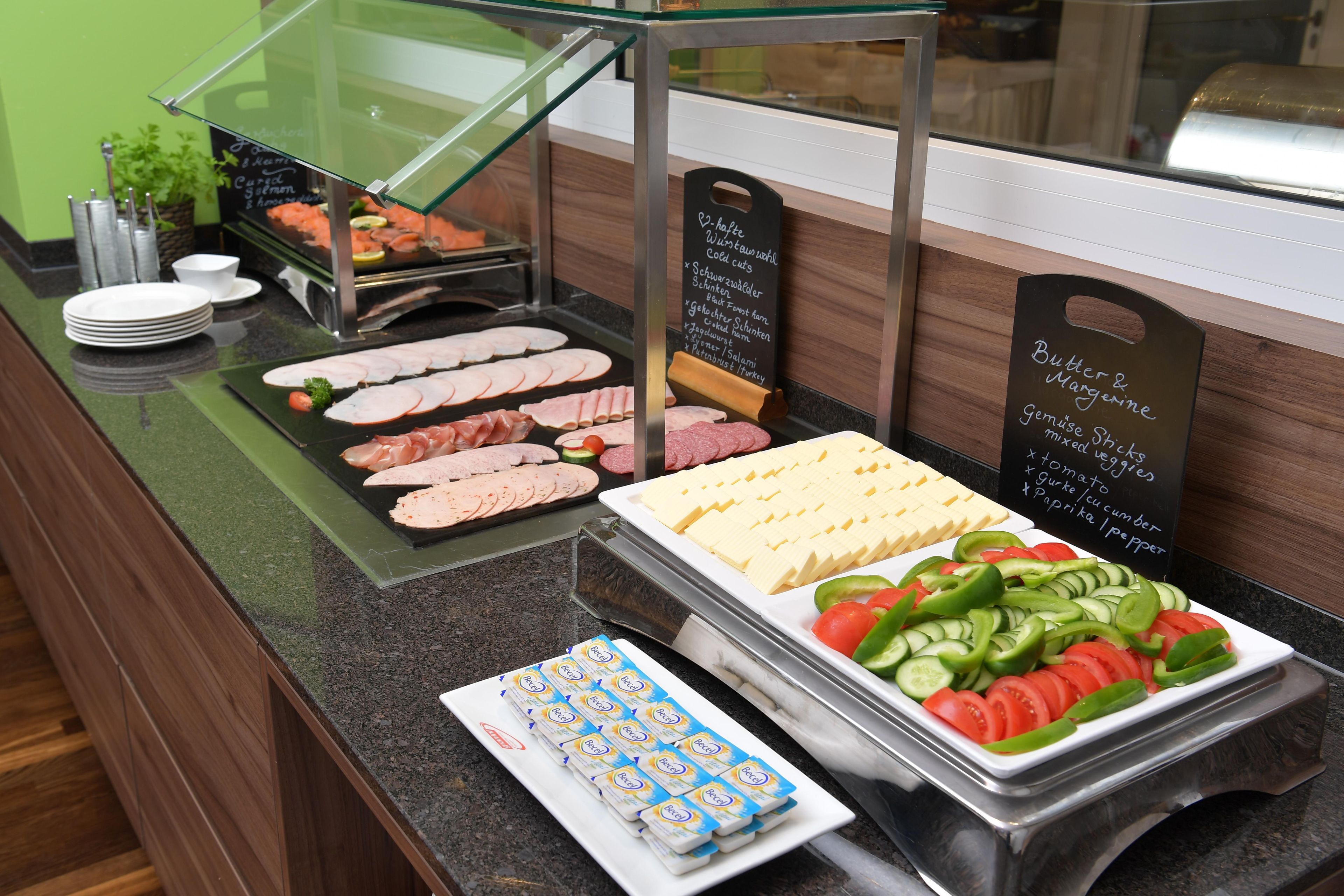 A buffet counter with various food options including sliced meats, cheese, and vegetables.