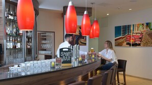 Una zona de bar con mostrador, taburetes y una estantería con botellas y vasos.