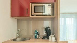 Eine kleine Küchenzeile mit Mikrowelle, Kaffeemaschine und Spüle.