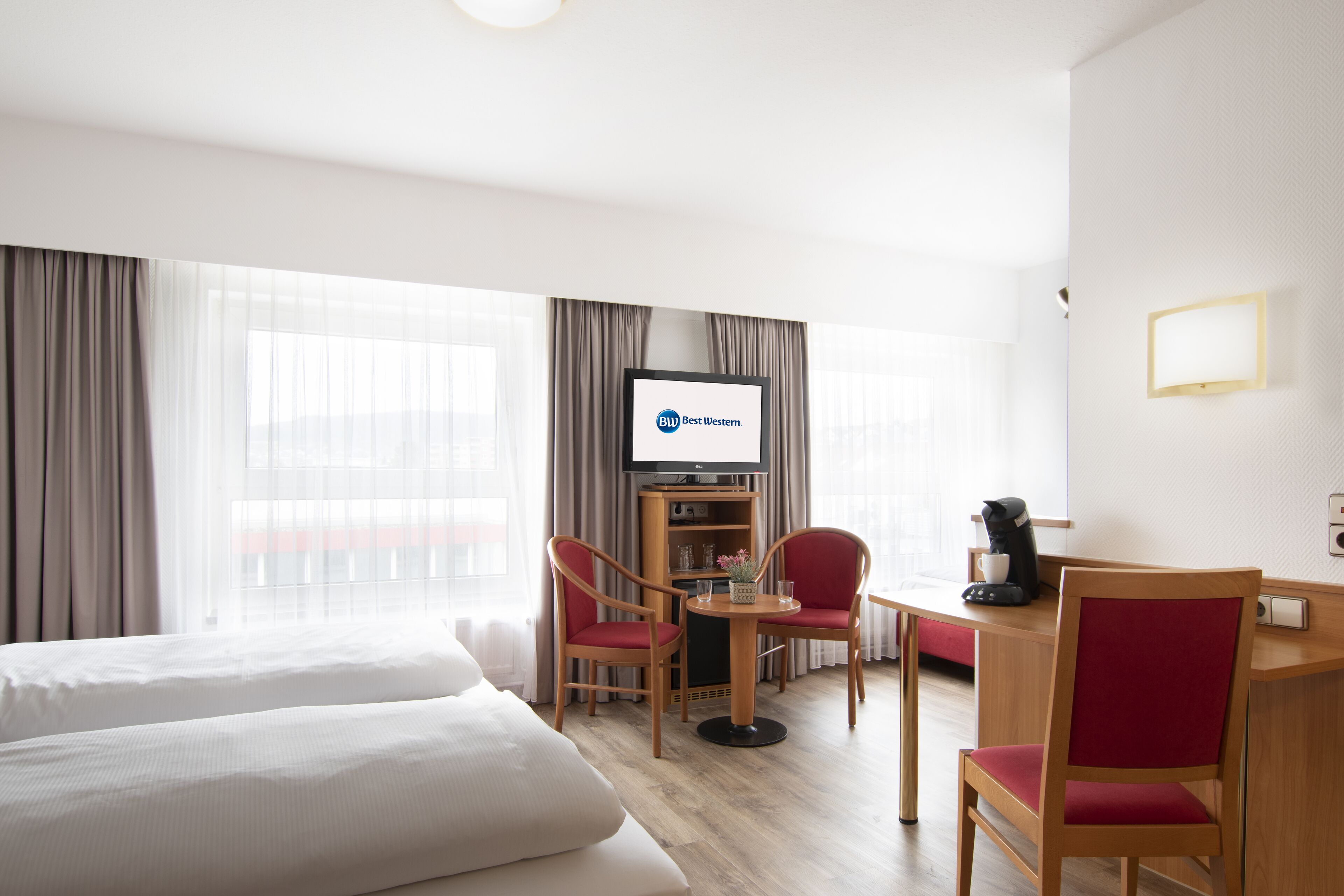 A hotel room with two beds, a desk with a coffee maker, a TV, and a bookshelf.
