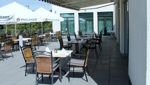 An outdoor patio with tables and chairs, umbrellas, and a white building with large windows. - Best Western Queens Hotel Pforzheim-Niefern (Niefern)