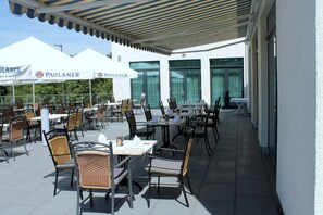 An outdoor patio with tables and chairs, umbrellas, and a white building with large windows. - Best Western Queens Hotel Pforzheim-Niefern (Niefern)