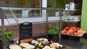 Exhibición de queso y fruta con un cartel que indica precios y tipos de queso.