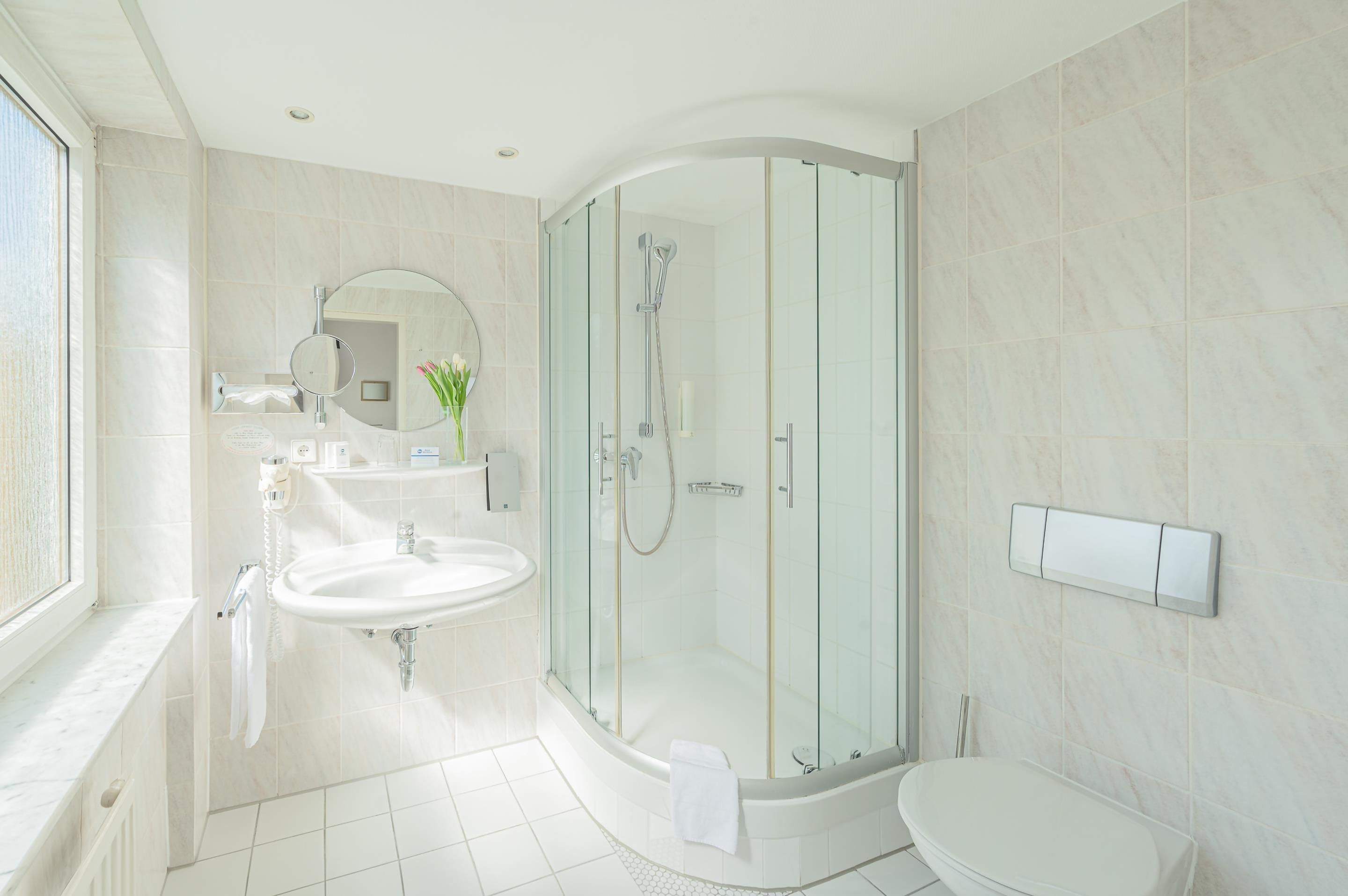 Un baño moderno con ducha envuelta en vidrio, un lavamanos blanco y un inodoro.