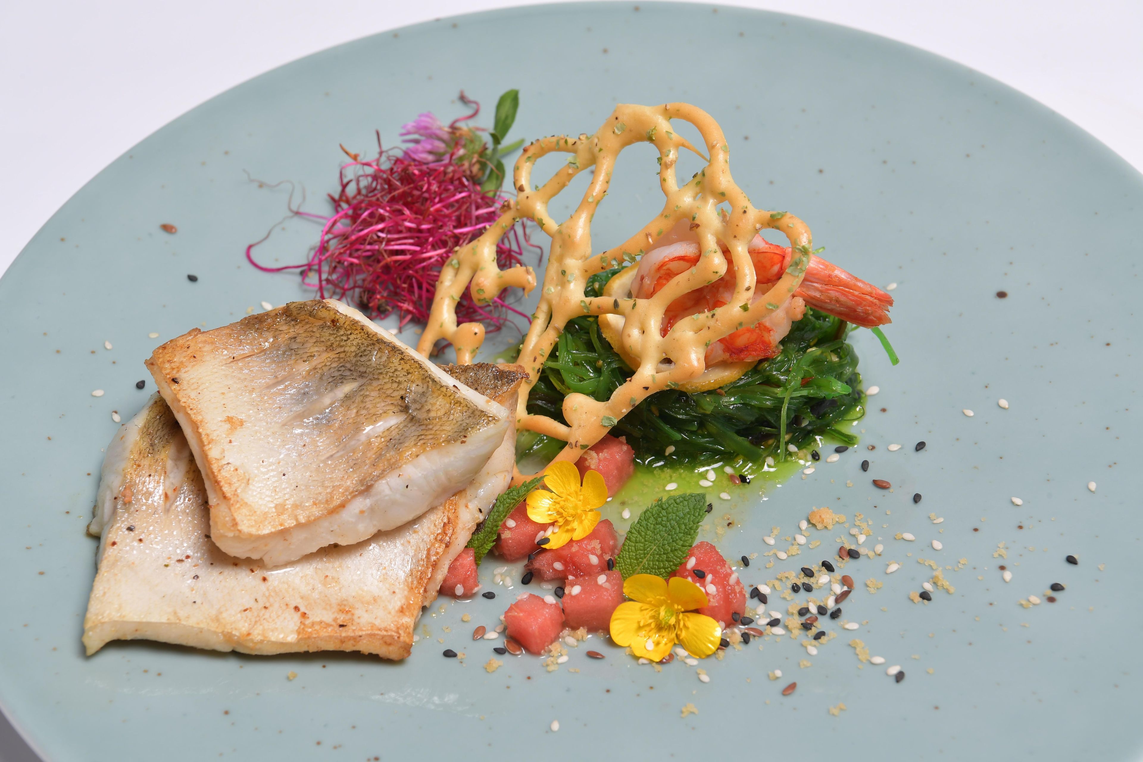 Une assiette comprenant un morceau de poisson grillé, une tranche de pain et une salade garnie de divers ingrédients.