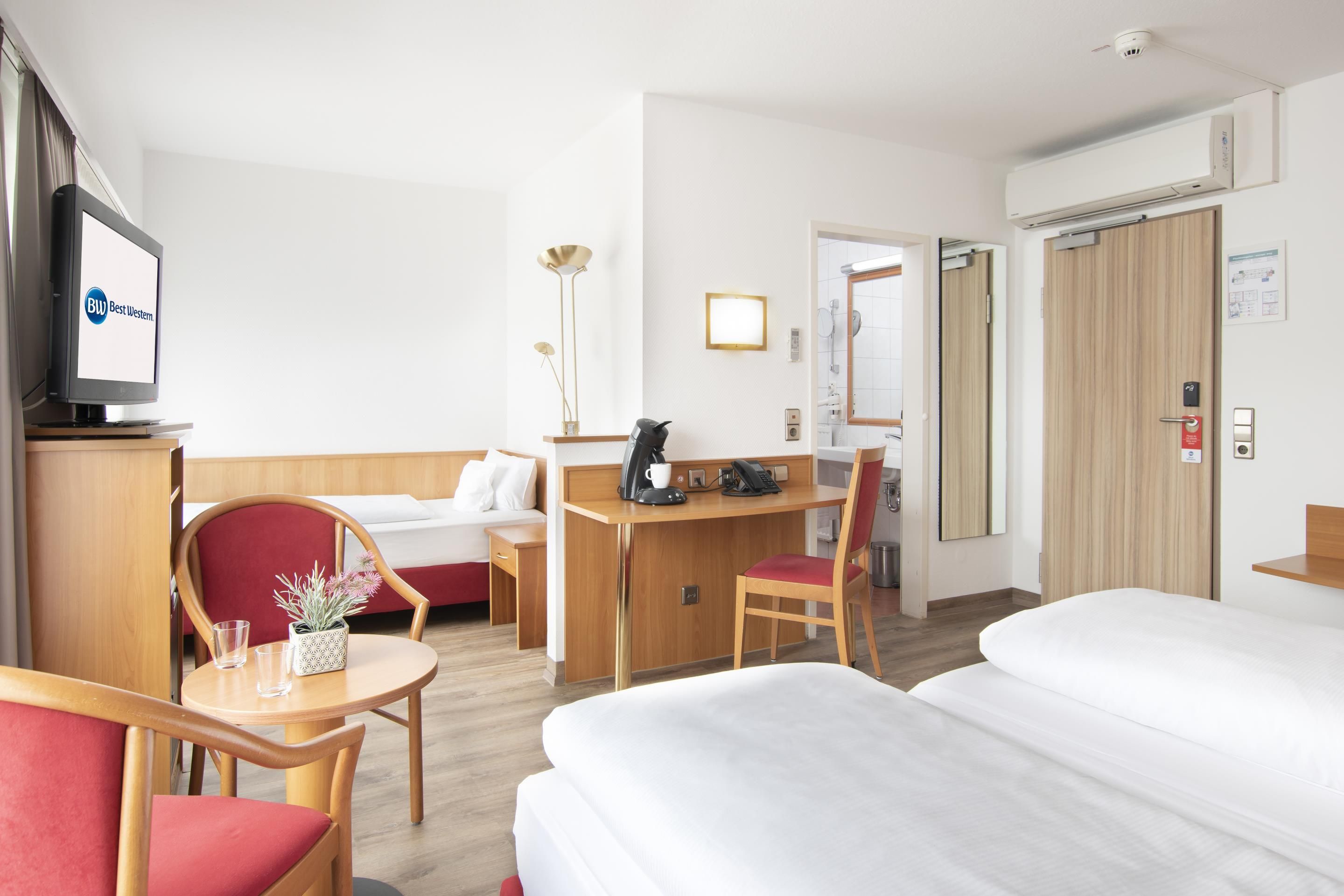 Ein Hotelzimmer mit einem Bett, einem Schreibtisch, einem Sessel, einem Fernseher und einem Nachttisch mit Pflanze.