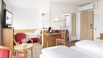 Ein Hotelzimmer mit einem Bett, einem Schreibtisch, einem Sessel, einem Fernseher und einem Nachttisch mit Pflanze.
