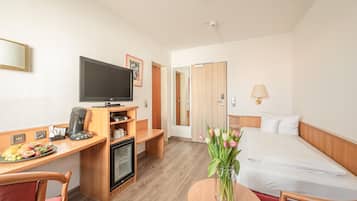 A hotel room with a bed, a desk with a television, a coffee machine, and a vase with flowers.