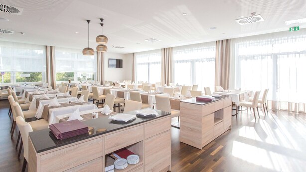 Un comedor espacioso con varias mesas y sillas, ventanas amplias y un diseño moderno de techo.